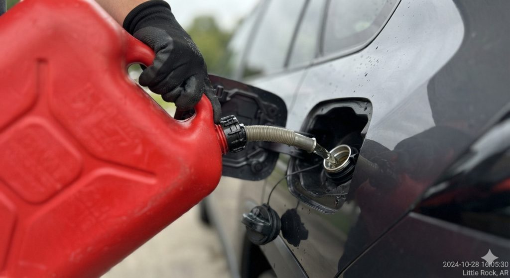 Roadside technician filling a red safety gas can into a stalled vehicle on a road shoulder in Little Rock, AR.